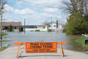 Photo shows a "road closed" sign with a flooded town street in the background