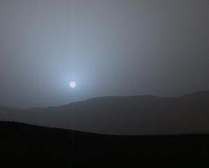 Four images taken over the course of 6 minutes and 51 seconds showing the setting sun on Mars. In the distance is a gentle slope.