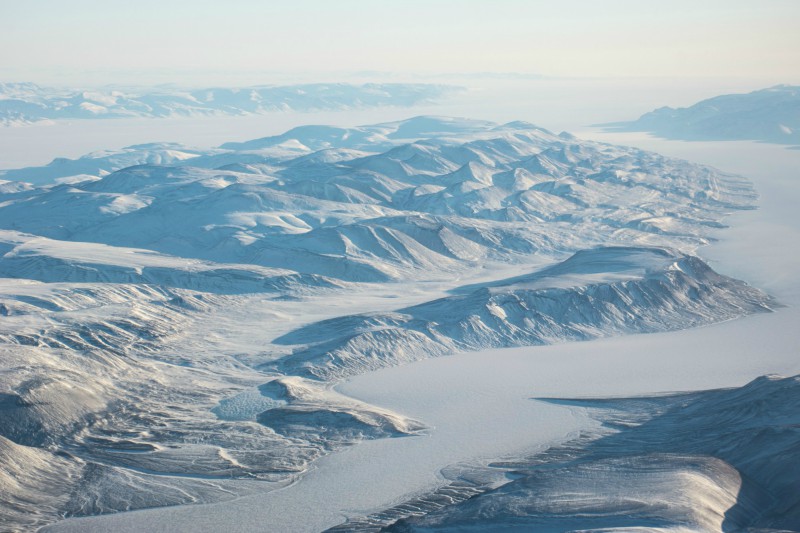 Photo shows an aerial long-distance view of a snow and ice landscape, mountains and a river channel, near the PEARL ridge lab at Eureka.