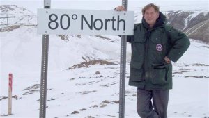 A photo of Jim Drummond, standing in an ARctic landscape at a sign that reads 80 degrees north