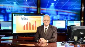Photo shows a smiling weathercaster, Jim Gandy, sitting at a desk with several screens behind him, for the article by Bronwyn McIlroy-Young