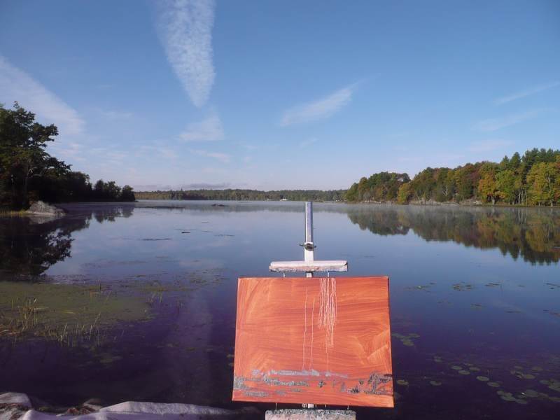 Red base canvas on an easel by a lake an blue skies with clous overhead