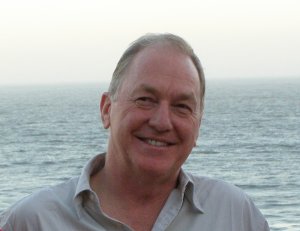 Causasian male smiling looking off to his right with an ocean and white sky behind him